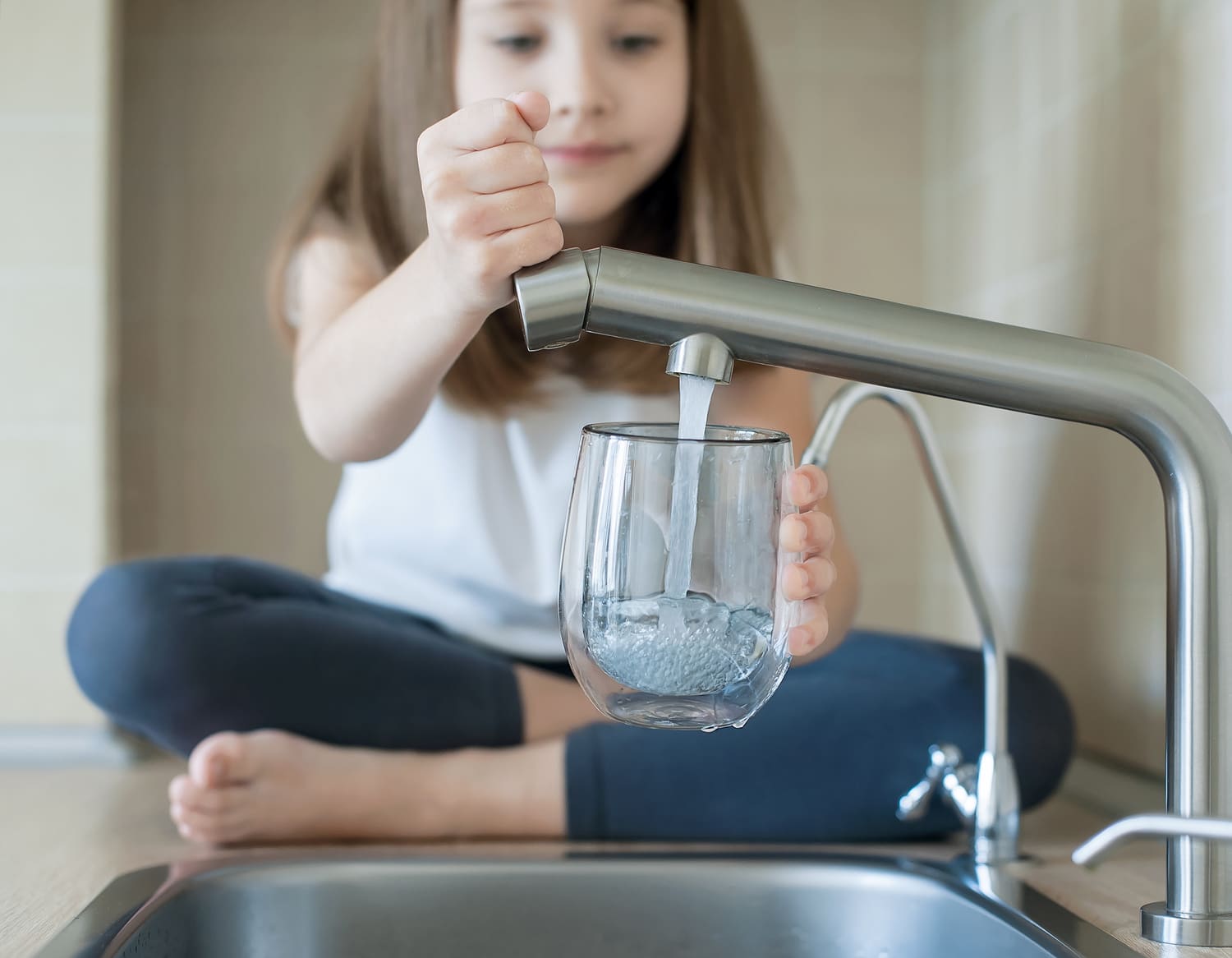 Little girl open a water tap with her hand holding a transparent