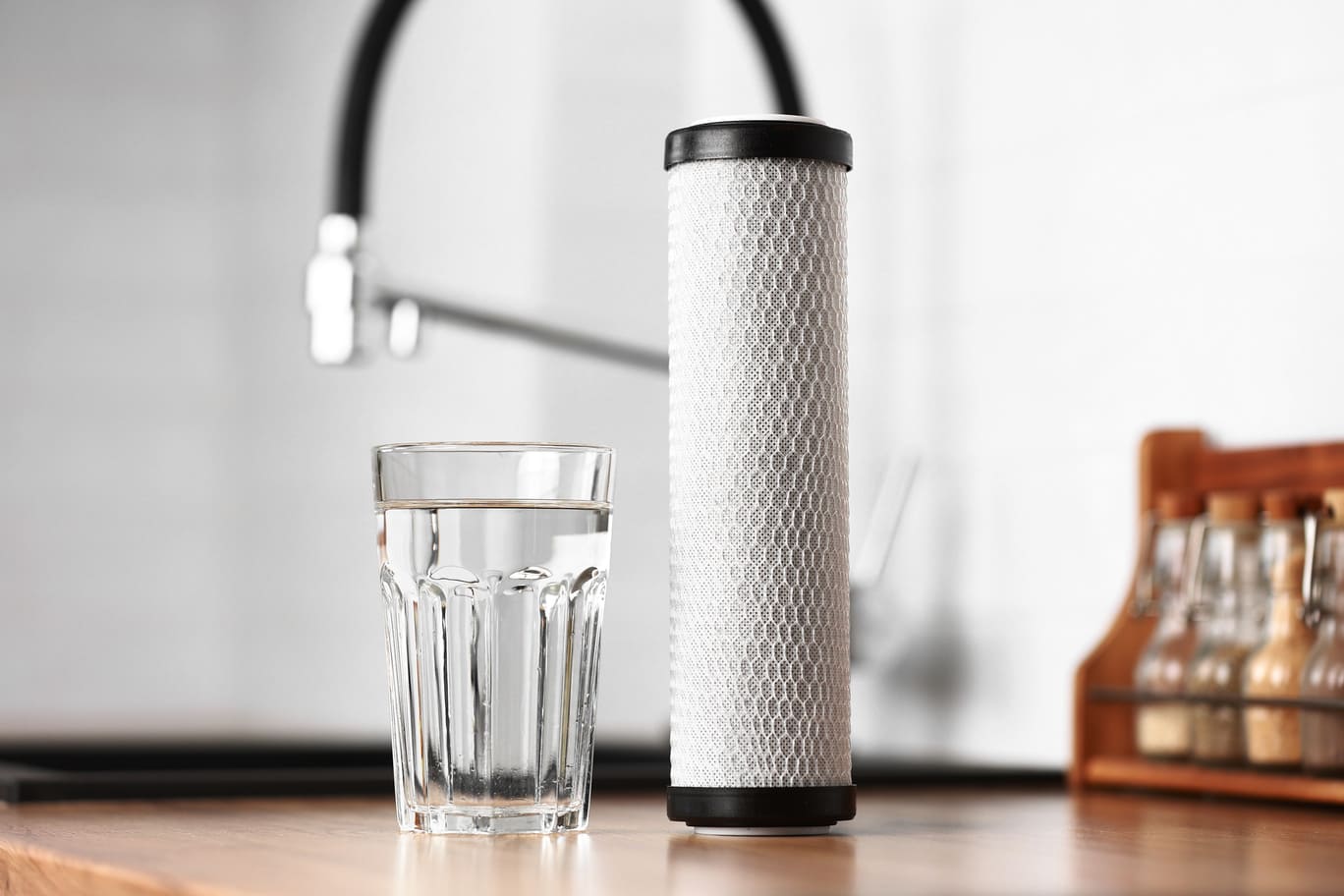 A glass of clean fresh water and carbon filter cartridge on wooden table in a kitchen interior. Installation of reverse osmosis water purification system. Concept Household filtration system
