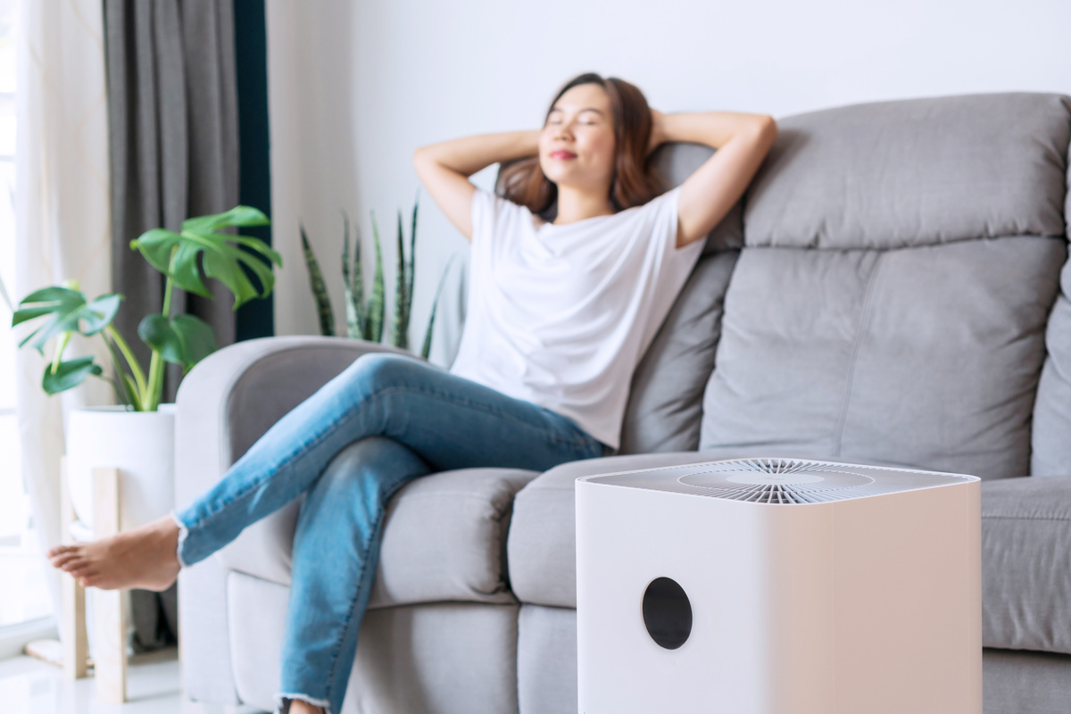 young woman on comfortable sofa, hands behind head rest at home wellbeing breathing fresh air from air purifier