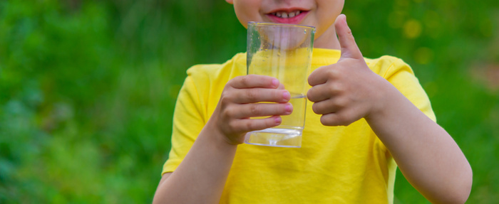 little boy drinking treated water with a glass.