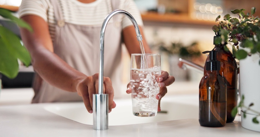 Hands, glass and water by faucet in kitchen for hydration, thirst or wellness in morning at apartment. Person, container and pouring filtered water from sink with tap