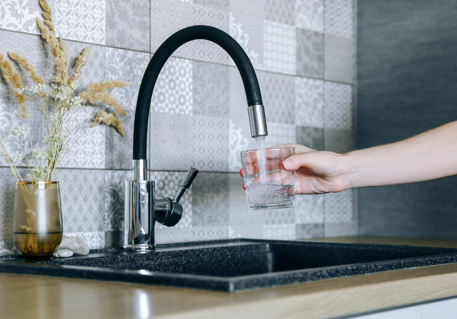 Human hand holding glass pouring fresh drink water at kitchen faucet
