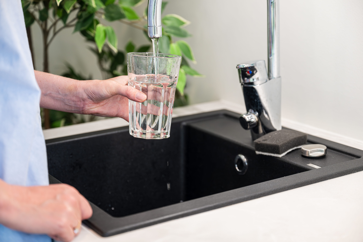 Woman pouring filtered water into a glass from the tap in the kitchen