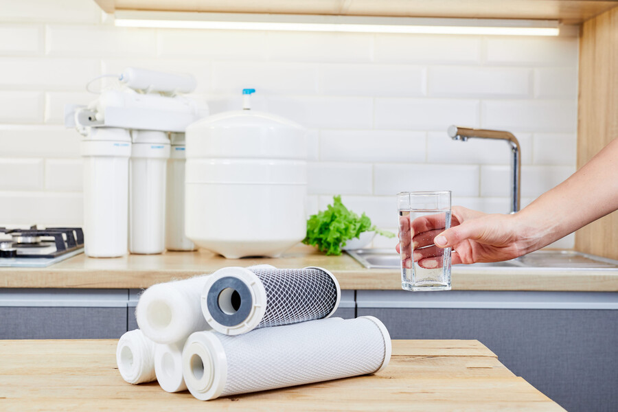 Woman holding glass of pure water at table in kitchen
